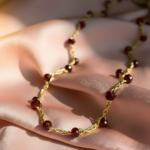 Collana artigianale dorata con piccole perline rosso bordeaux distribuite lungo la catena, gioiello elegante e minimal.