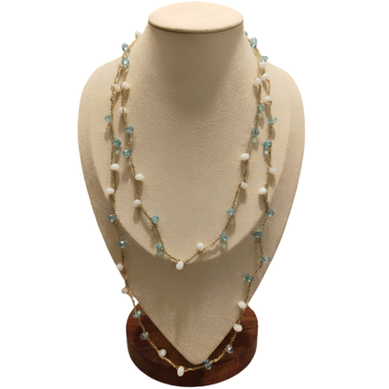 Collana artigianale lunga con catena dorata e pietre in pasta di vetro bianche e celesti, disposta su busto espositivo beige
