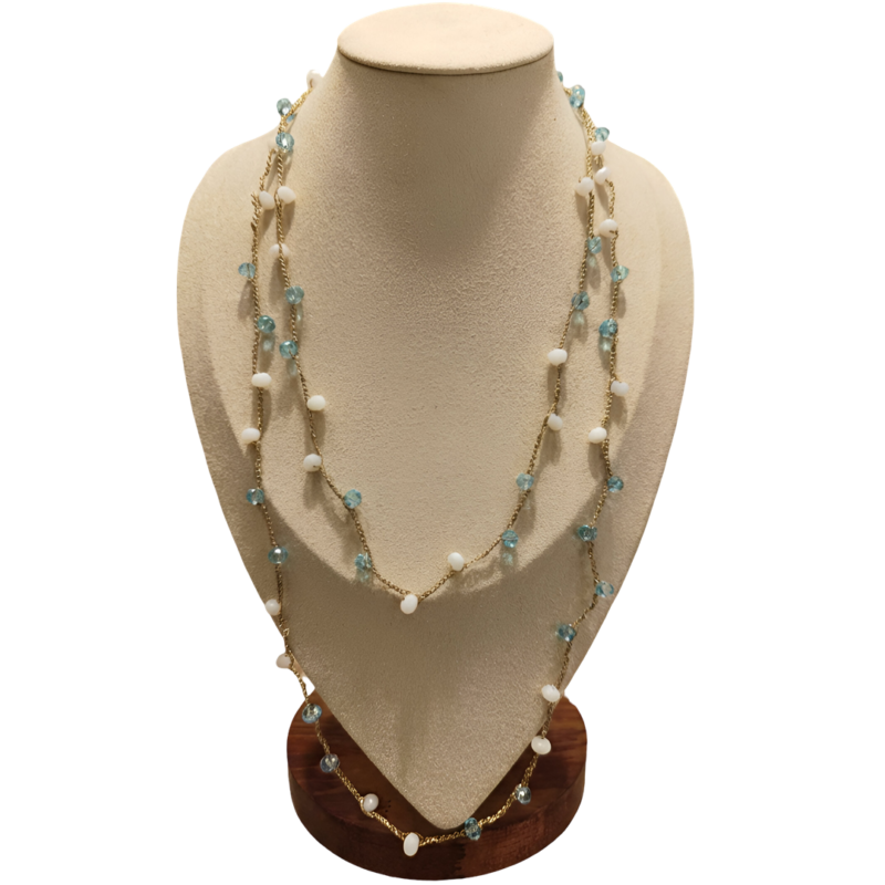 Collana artigianale lunga con catena dorata e pietre in pasta di vetro bianche e celesti, disposta su busto espositivo beige